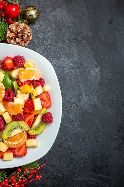 Foto gratuita metà colpo di raccolta di frutta fresca su accessori per la decorazione del piatto da cena rami di abete su sfondo scuro