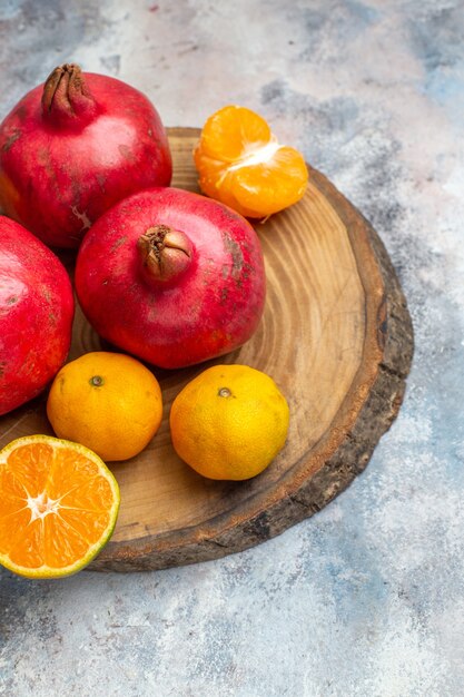 Half shot of collection of fresh fruits with pomegranates oranges and tangerines on a wooden tray on ice background