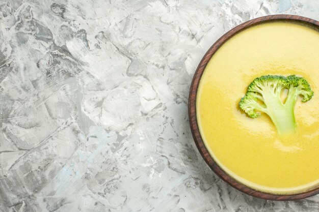 Half shot of cream of broccoli soup in a brown bowl on white table