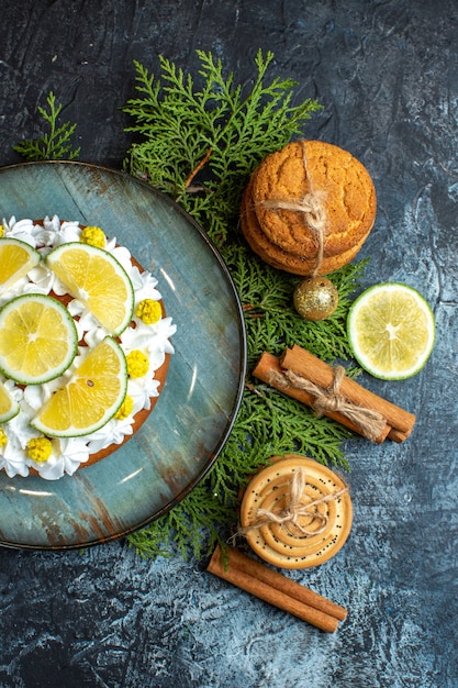 Half shot of creamy delicious cake and fir branches lemon cinnamon limes on dark background