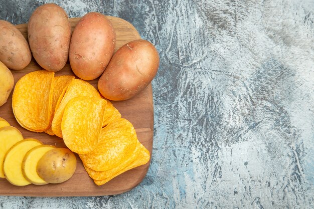 Half shot of crispy chips and uncooked potatoes on wooden cutting board on gray table