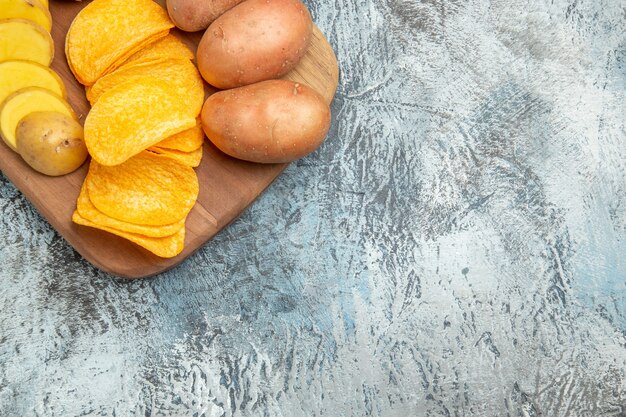 half shot of crispy chips and uncooked potatoes on wooden cutting board on gray table