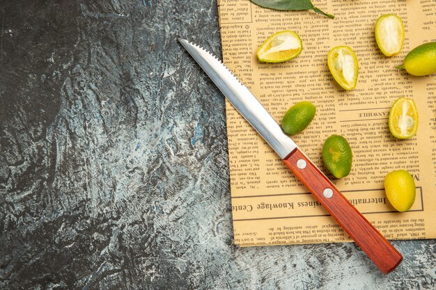 Half shot of cut in half fresh kumquats and knife on newspapers on gray background