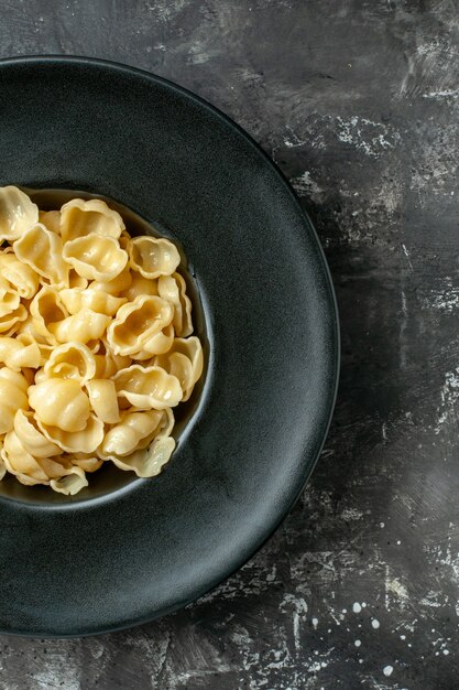 Half shot of delicious conchiglie on a black plate on gray background