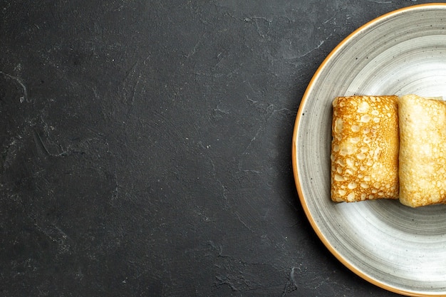 Half shot of delicious meat-filled pancakes on a white plate on black background