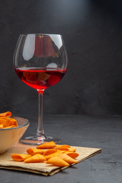 Half shot of delicious potato chips inside and outside the bowl and red wine in a glass on an old newspaper