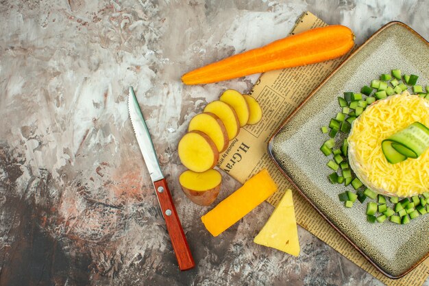 Half shot of delicious salad on an old newspaper and two kinds of cheese and carrots chopped potatoes on mixed color table