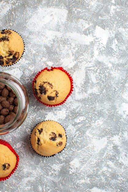 Half shot of delicious small cupcakes and chocolate in a glass pot next to Christmas gift on the right side on ice table in vertical view