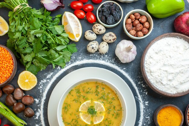 Half shot of delicious soup served with lemon and green in a white bowl and flour tomato oil bottle flour green bundles eggs on dark