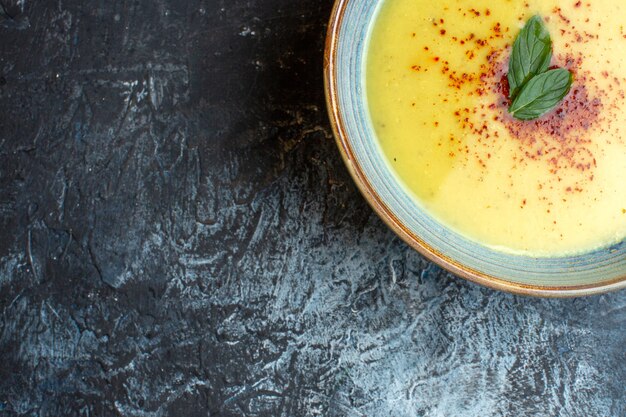 Half shot of delicious soup served with pepper and mint in a blue pot on the left side on dark background