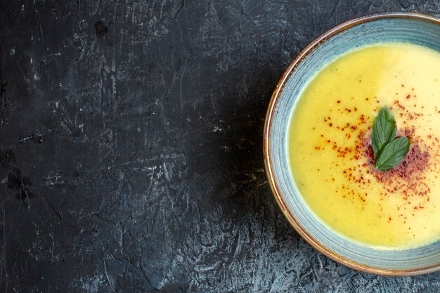 Половина шота вкусного супа с перцем и мятой в синей кастрюле слева на темном фоне
