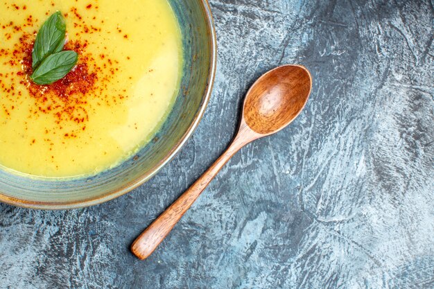 Half shot of delicious soup served with pepper and mint in a blue pot next to wooden spoon on dark background