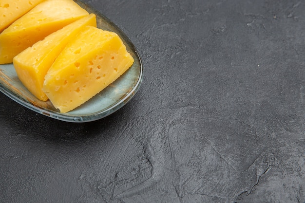 Free photo half shot of delicious yellow sliced chees on a blue plate on the right side on black background