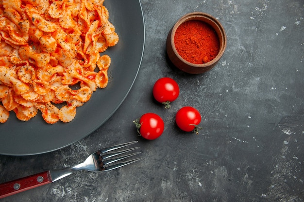 Free photo half shot of easy pasta meal for dinner on a black plate and fork pepper and tomatoes on a dark background