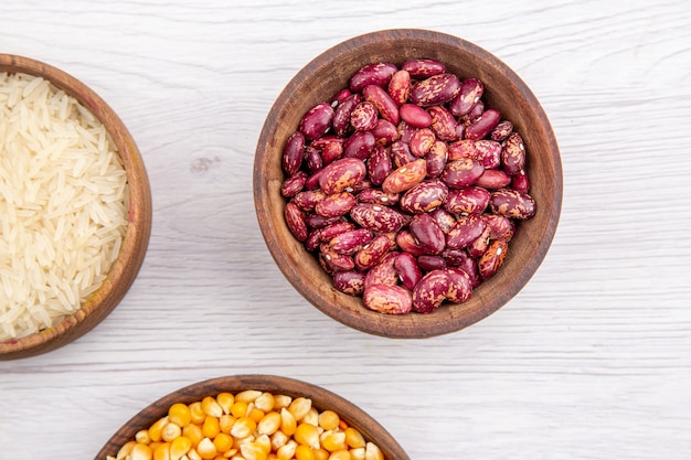 Half shot of fresh beans and rice corn kernels yellow lentils in brown bowls on white table in above view