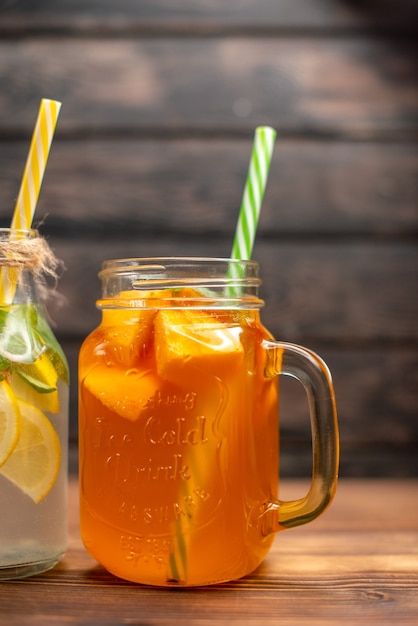 Half shot of of fresh detox water and fruit juice served with tubes on the left side on a brown background