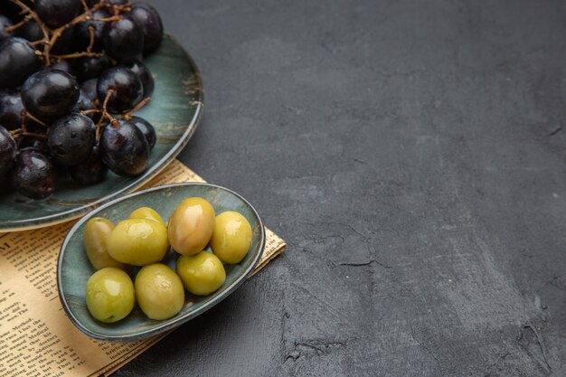 Half shot of fresh organic green olives and bundles of black grape on an old newspaper on a dark background