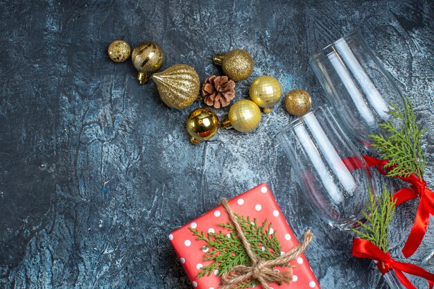 Half shot of glass goblets with red ribbon and decoration accessories next to gift boxes on dark table