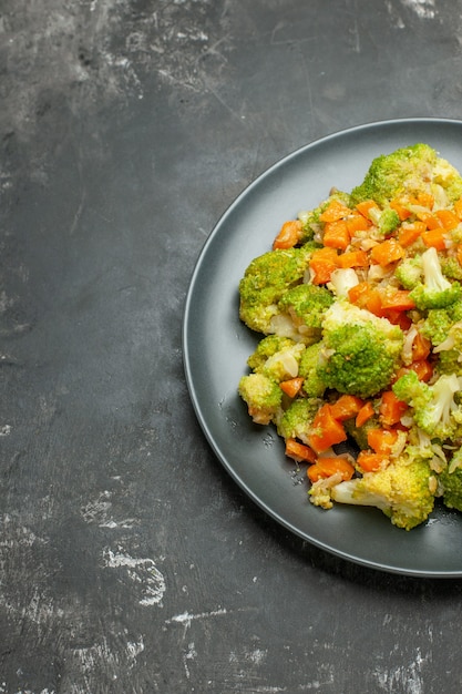 Free photo half shot of healthy meal with brocoli and carrots on a black plate on gray table