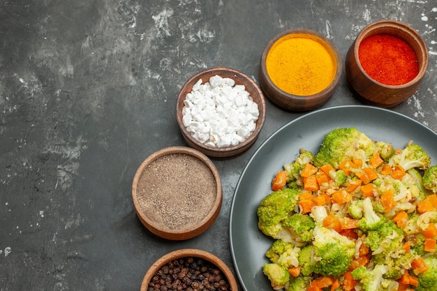 Mezzo colpo di pasto sano con broccoli e carote su un piatto nero e spezie sul tavolo grigio