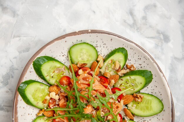 Half shot of homemade healthy delicious vegan salad decorated with chopped cucumbers in a bowl on stained white surface with free space