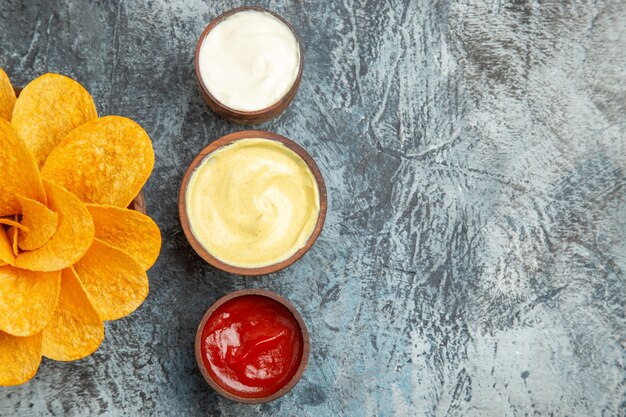 Half shot of homemade potato chips decorated like flower shaped and salt with ketchup mayonnaise on gray table
