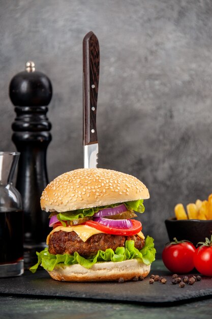 Half shot of knife in delicious meat sandwich and green pepper on black tray sauce ketchup tomatoes with stem fries on dark surface