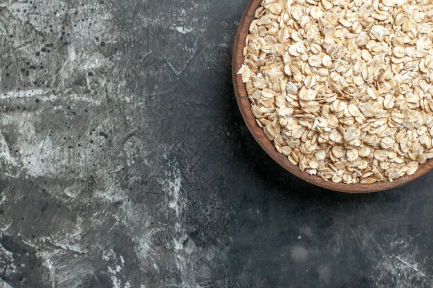 Half shot of organic oat bran in a brown wooden pot on dark background