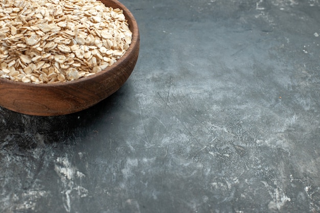 Half shot of organic oat bran in a brown wooden pot on the right side on dark background