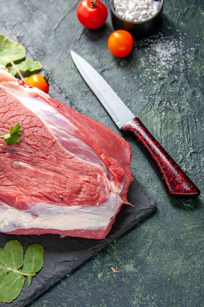 Half shot of raw fresh red meat and greens on cutting board knife tomatoes on green black mix colors background