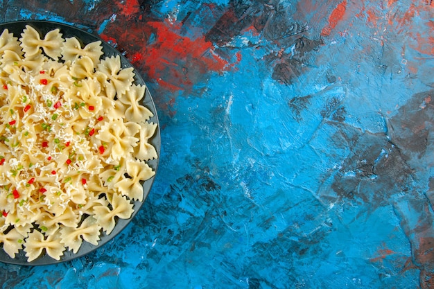 Half shot of of raw Italian farfalle pasta with vegetables on the right side on blue background