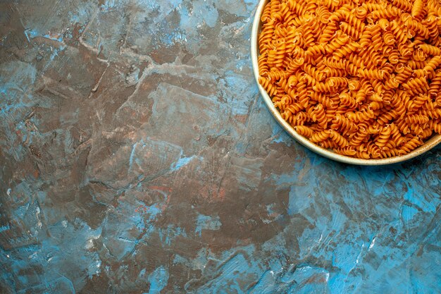 Half shot of raw Italian pastas in a white bowl on blue background in above view