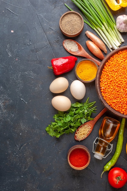 Half shot of red lentil in a brown pot among organic vegetables eggs fallen oil bottle on black