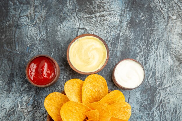 Half shot of tasty potato chips decorated like flower shaped and salt with ketchup mayonnaise on gray table