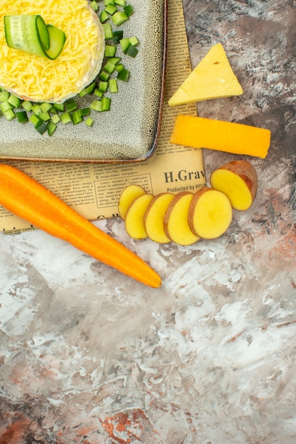 Half shot of tasty salad on an old newspaper and two kinds of cheese and carrots chopped potatoes on mixed color table