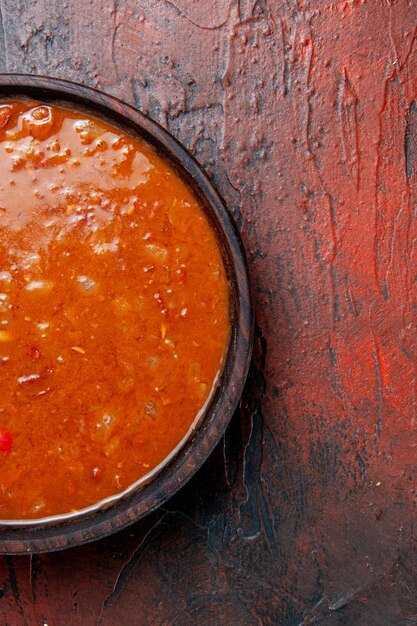 Half shot of tomato soup in a brown bowl on the left side of mixed color table 