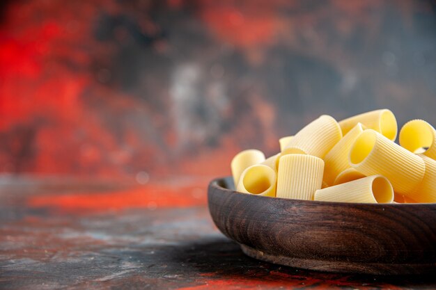 Half shot of uncooked pastas in a brown bowl on a dark table