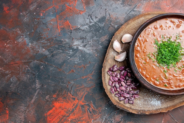 Half shot of view of tomato soup beans garlic on wooden cutting board on mix color table