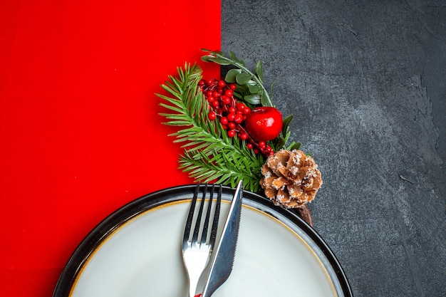 어두운 테이블에 빨간 냅킨에 디너 플레이트 장식 액세서리 전나무 가지에 빨간 리본으로 설정 칼 붙이 크리스마스 배경의 절반 샷