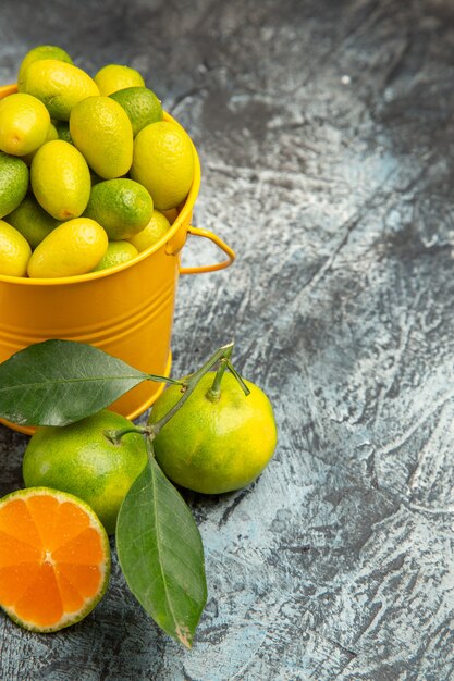 Half shot of a yellow bucket full of fresh green tangerines and cut in half tangerines on gray background