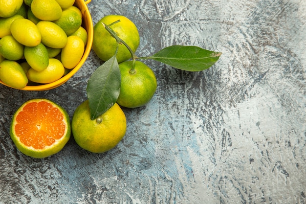 Half shot of a yellow bucket full of fresh green tangerines and cut in half tangerines on gray background