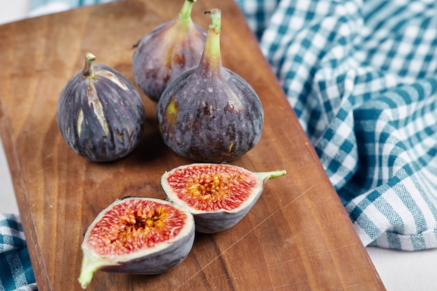 Half slices and whole figs on wooden board with a blue tablecloth.