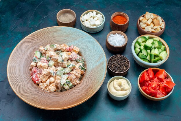 Half-top mayyonaise vegetable salad inside plate along with sliced vegetables and seasonings on dark desk, food meal vegetable salad