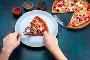 Free photo half-top view baked delicious pizza with olives sausages and cheese female eating it on blue desk.