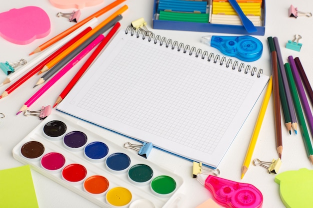 Цветные карандаши с красками и наклейками на белом столе, вид сверху, рисование цветной краской