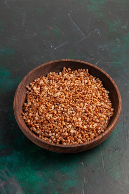 Half-top view cooked buckwheat tasty meal inside brown plate on the dark green surface