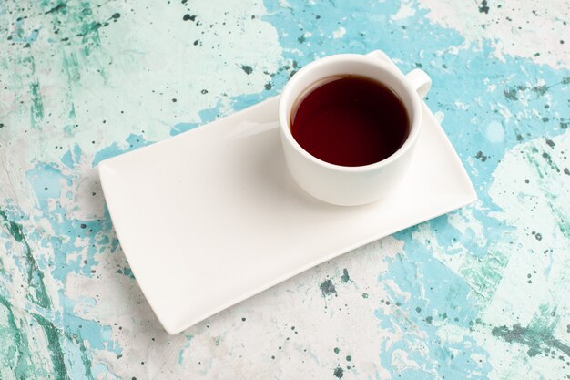 Half-top view cup of tea inside cup and plate on light-blue desk