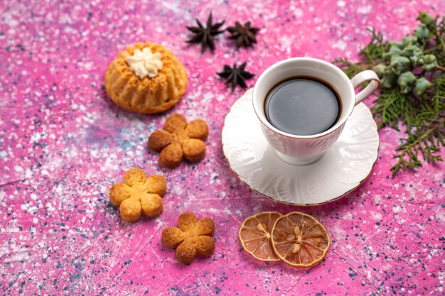 Half-top view cup of tea with little cake and cookies on the light-pink desk.