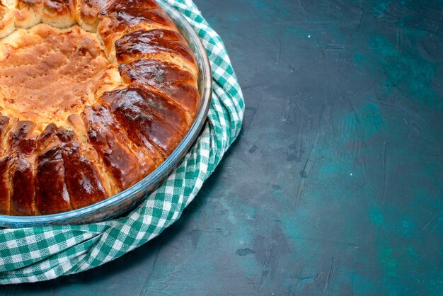 Вкусный испеченный пирог с видом на половину сверху и сладкий внутри стеклянной сковороды на голубом столе.