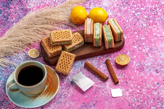 핑크 책상에 레몬 티와 계피와 함께 하프 탑보기 맛있는 샌드위치 쿠키.